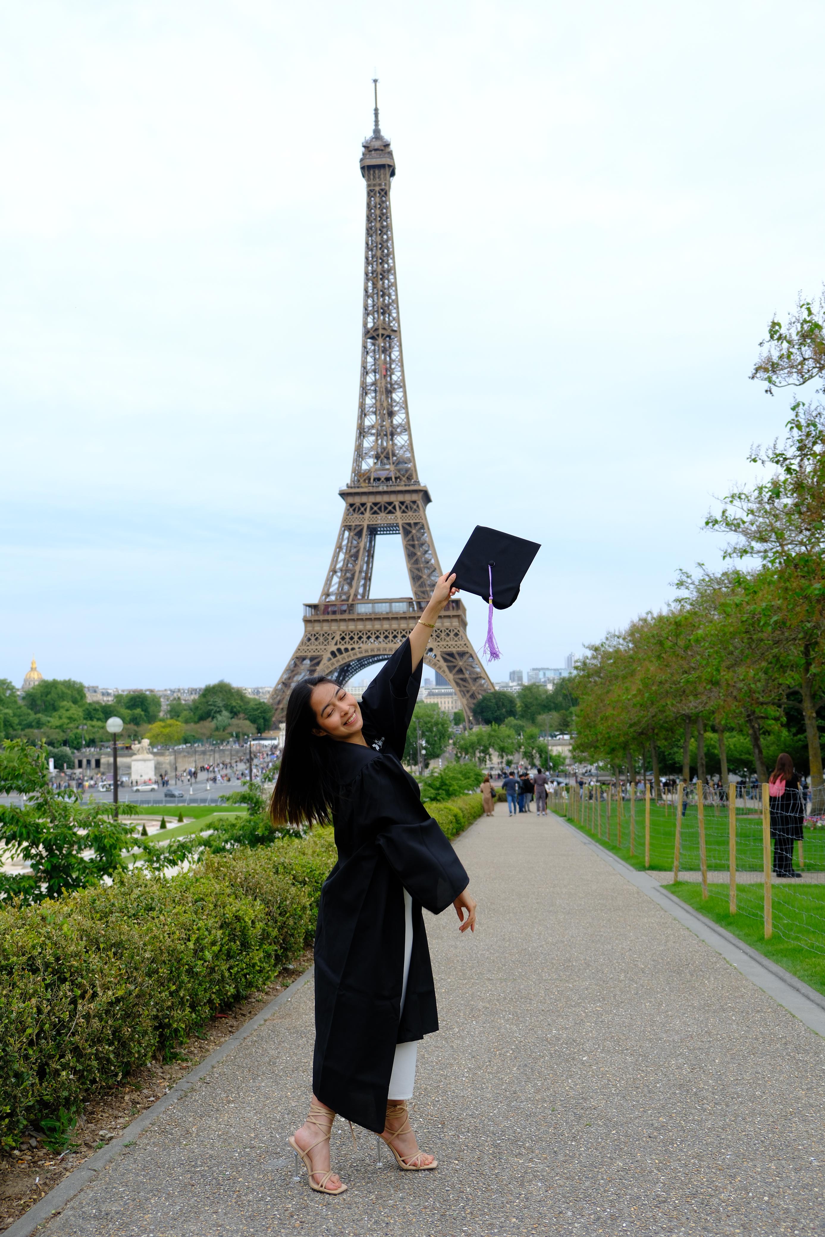 A graduate throws her cap in front of the Eiffel Tower after graduating from PPA Business School