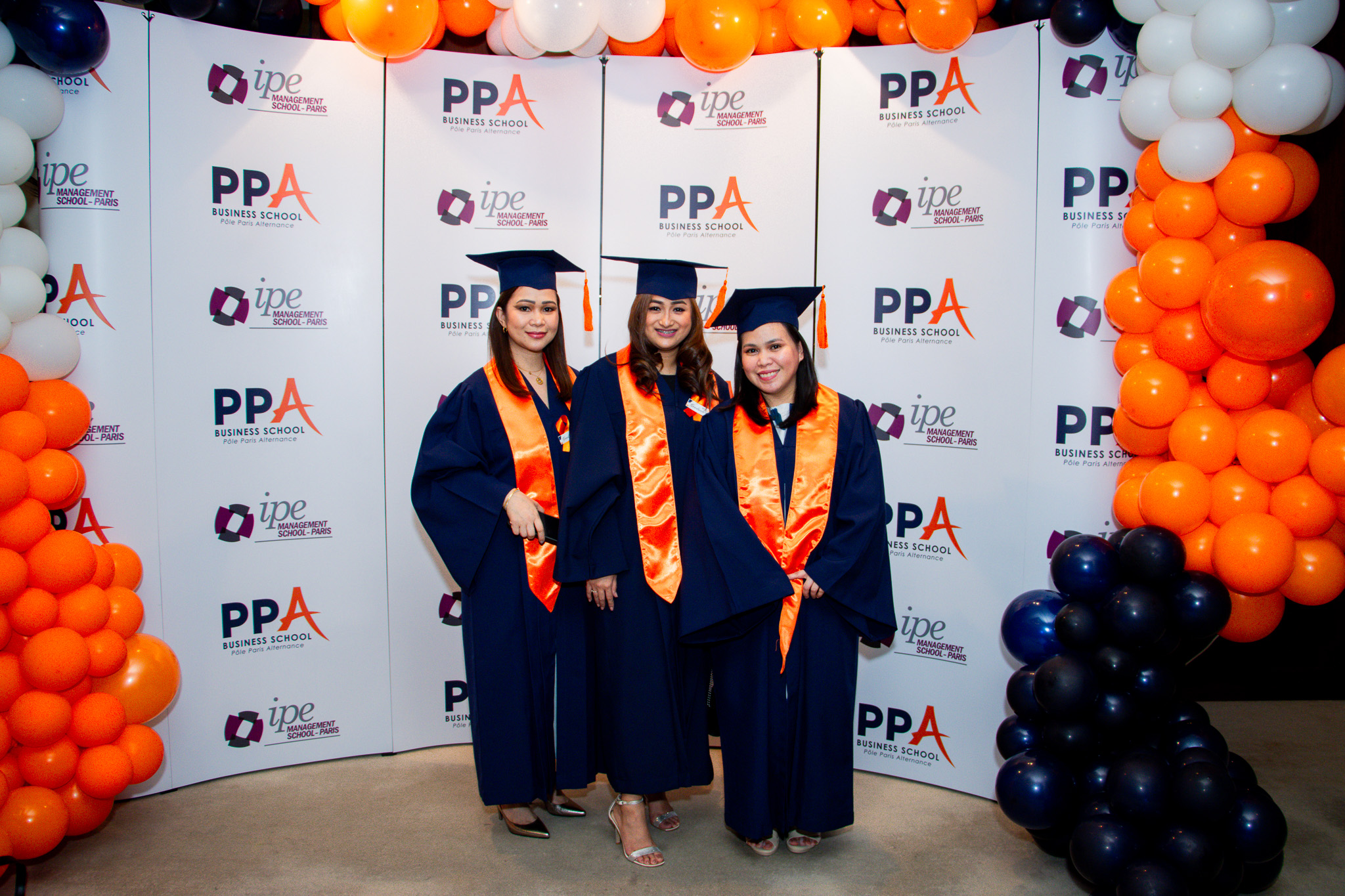 Three graduates smiling together in front of the PPA Business School and IPE Management School backdrop
