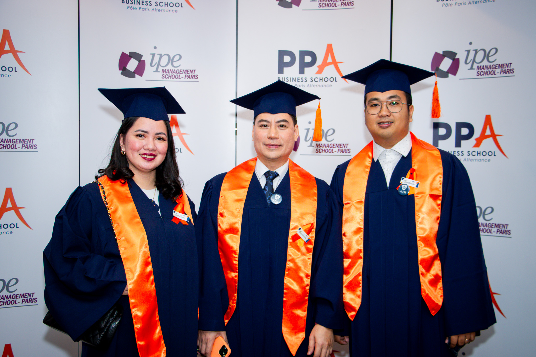 Three PPA Business School graduates smiling at the graduation photo backdrop
